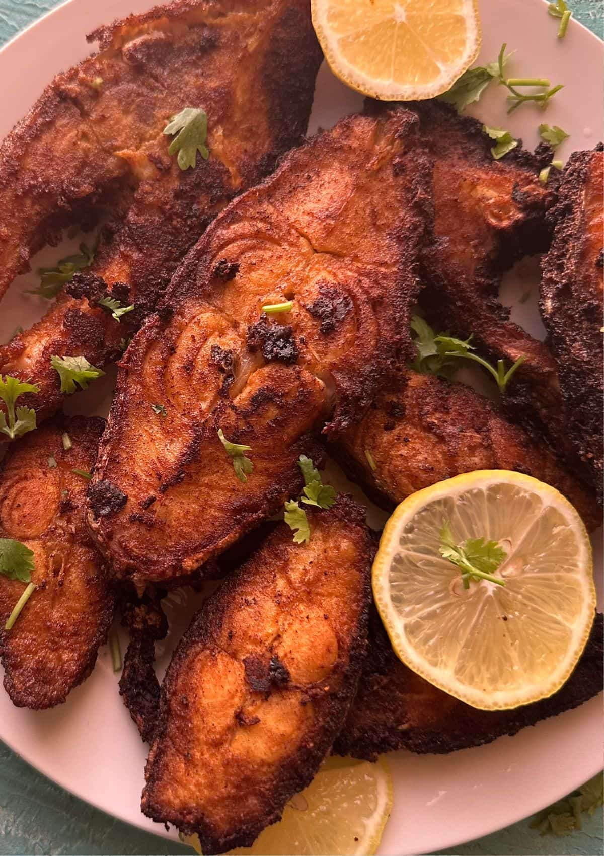 spicy fried fish served on a plate with lemon slices.