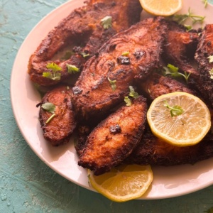 spicy fried fish served on a plate with lemon slices.