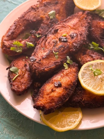spicy fried fish served on a plate with lemon slices.