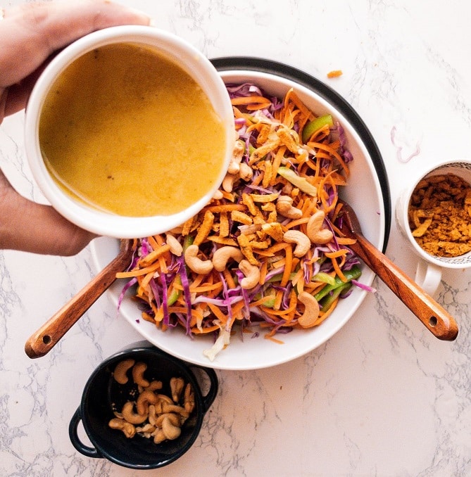Honey salad dressing pouring into a bowl of Cashews and vegetable salad