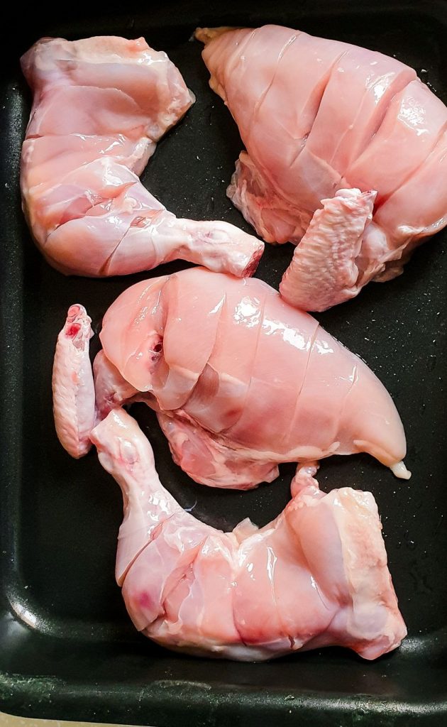 raw chicken pieces with cuts in a baking tray