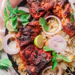 2 chicken tikka pieces sitting on a bed of rice in a black plate