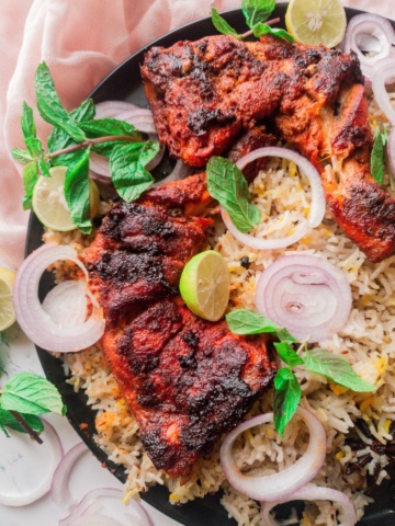 2 chicken tikka pieces sitting on a bed of rice in a black plate