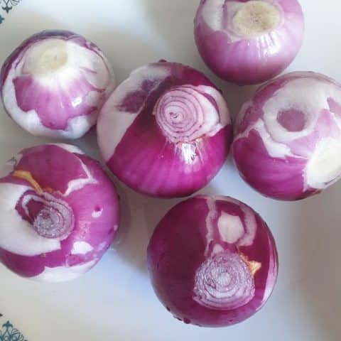 6 whole peeled red onions in a white plate