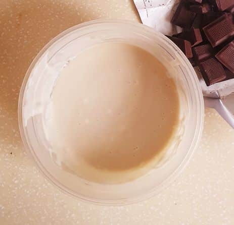 cream in a white plastic bowl with cup up chocolate cubes showing from the top right corner