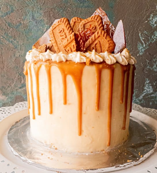 a front view of Lotus biscoff drip cake with caramel drip on a white iced cake, against a grey-blue backdrop