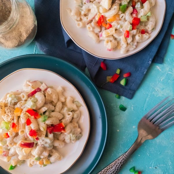 creamy pasta salad on two plates along with a fork on the side against a blue background