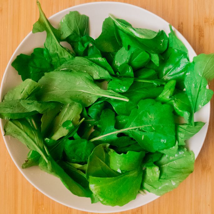 leafy greens (spinach) in a white bowl against a wooden backdrop