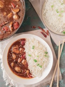 a plate containing half white rice and other half chicken sichuan curry. Chopsticks on the side and partial view of more rice and gravy
