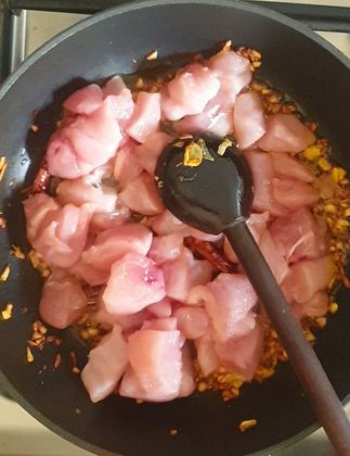 raw boneless chicken cubes tossed in a wok with oil and fried garlic and shallots, with a wooden spoon placed on top of it
