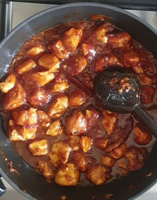 chicken cubes being sauteed in a wok with spicy Chinese sauces 