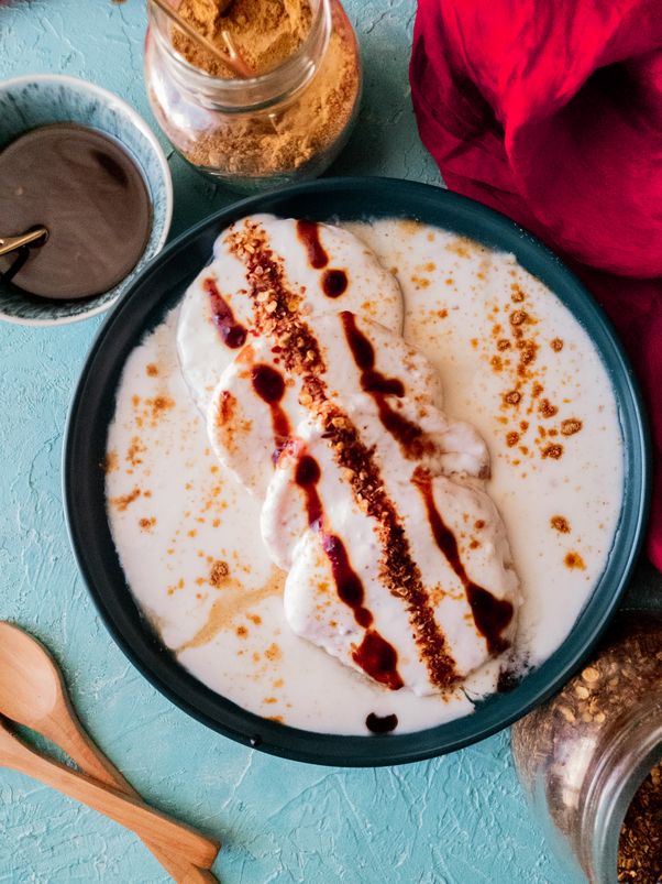 A green plate with 4 pieces of dahi baray in it with some yogurt sauce