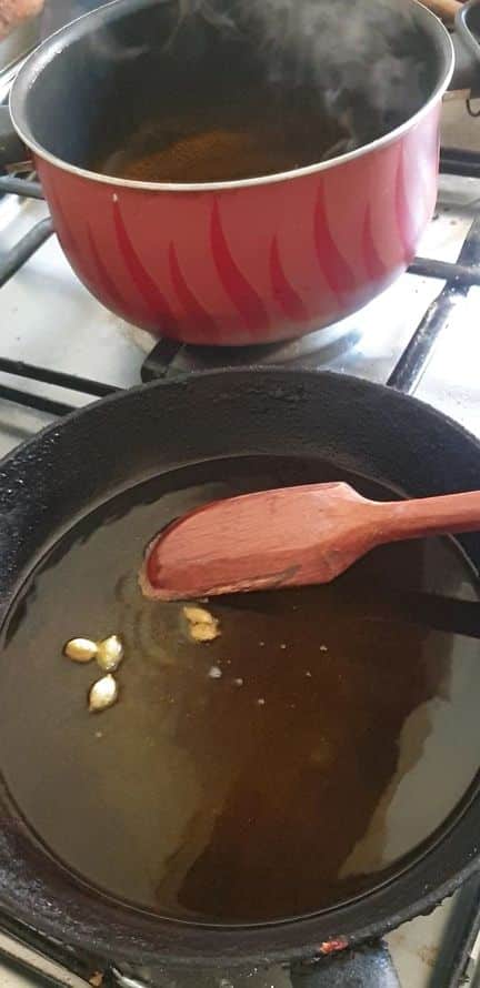 a black frying pan with some cardamom and liquid ghee in it and a wooden spoon