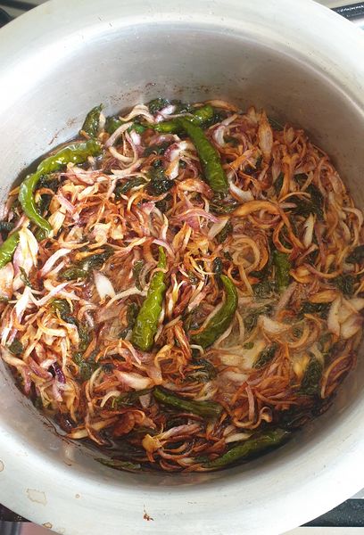 fried golden brown onions, green chilies and mint leaves in a pot