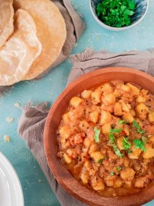 a partial view of a plate with aloo ki tarkari in it and a partial view of puri on the side
