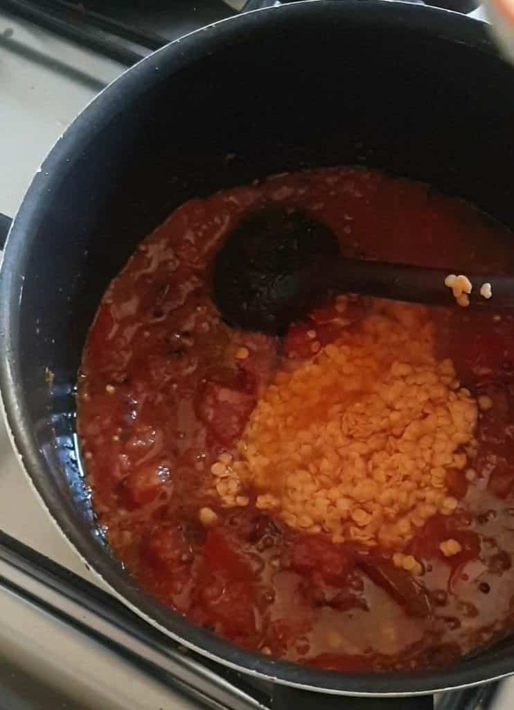 raw red lentils (masoor dal) in a black pot with a tomato based gravy