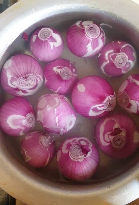 peeled red onions dipped in a container with water