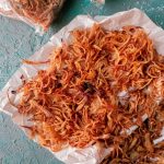 paper towel with lots of crispy golden brown onion slices on it against a grey background