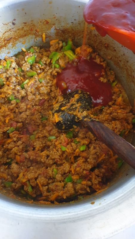 red sauce being added in a pot of minced beef and veggie