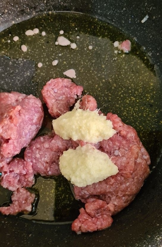 Raw minced meat with garlic ginger paste on top in a pool of oil in a black pan