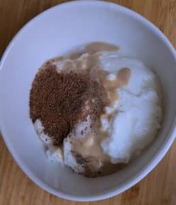 A white bowl containing yogurt, spices and tahini paste, all unmixed yet