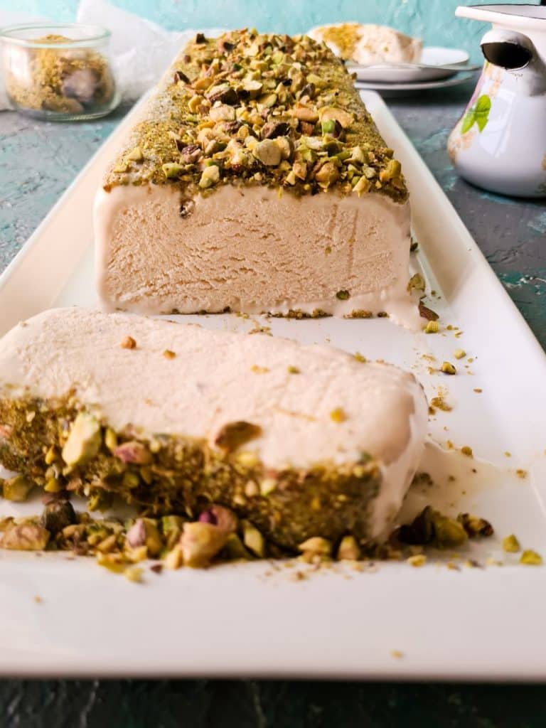 a slice of kulfi in a white dish topped with chopped pistachios