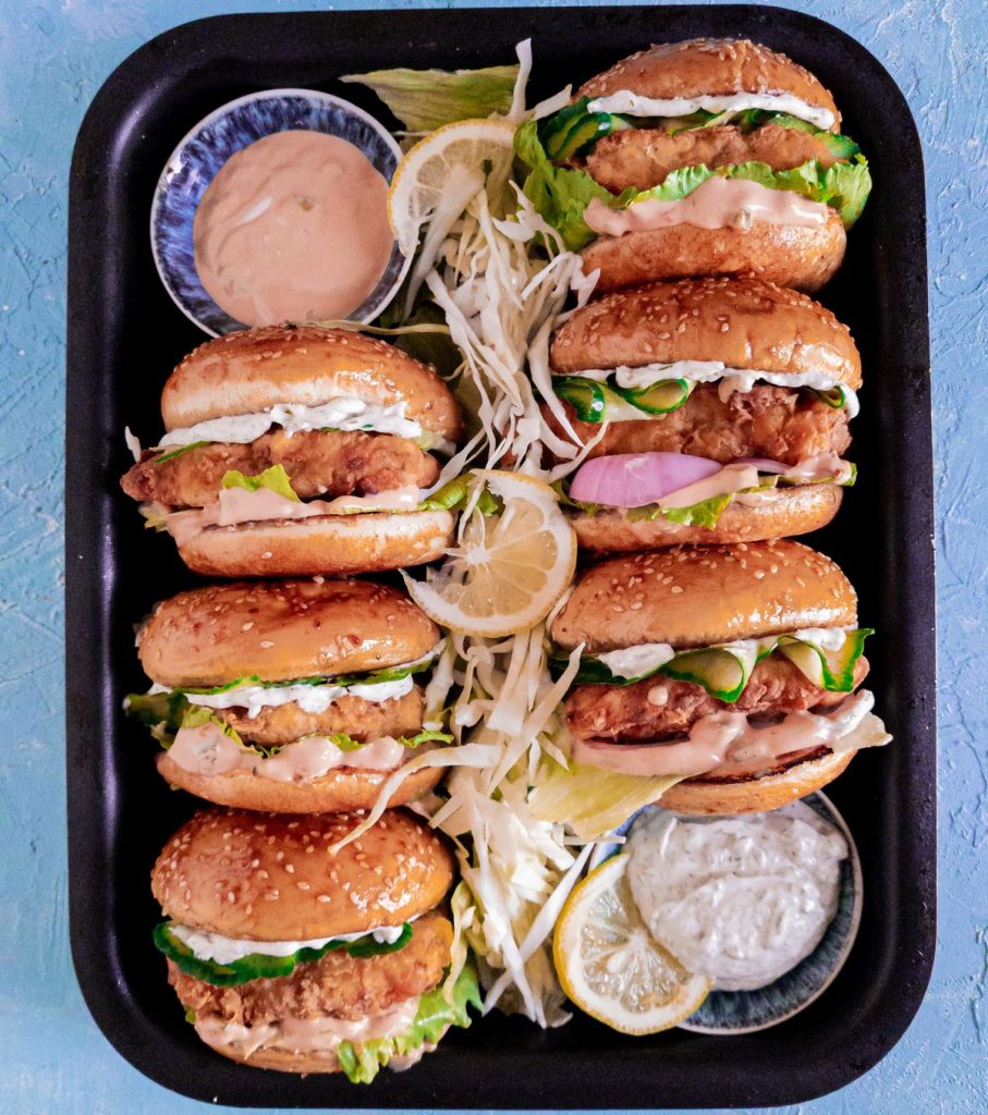 6 fish burgers in a black tray with tartar sauce and fry sauce on the side