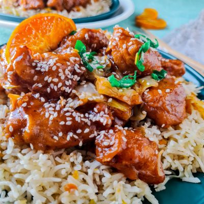 orange chicken with sesame seeds on top of a bed of rice