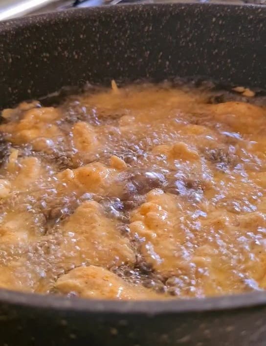 coated boneless chicken cubes being deep fried in oil