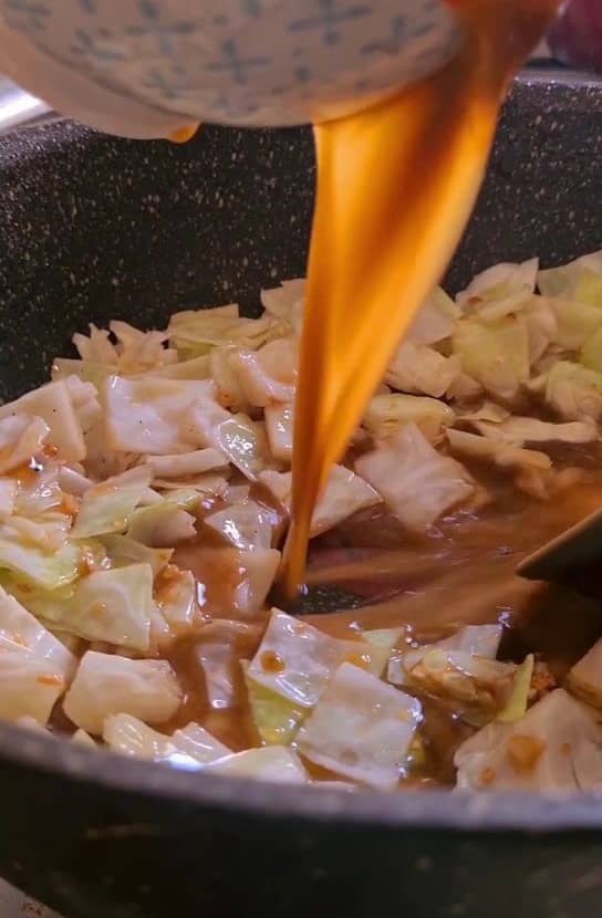 sauce being added in a pan containing chopped cabbage