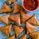 samosas laid on a blue paper with some ketchup on the side