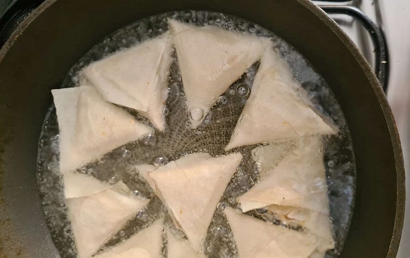 raw samosas frying in oil in a wok