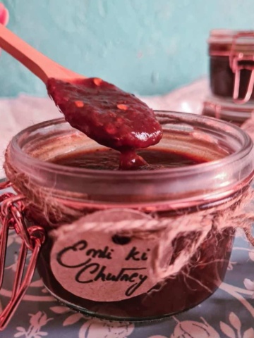 a wooden spoon taking out a spoonful of imli ki chutney in a labelled jar