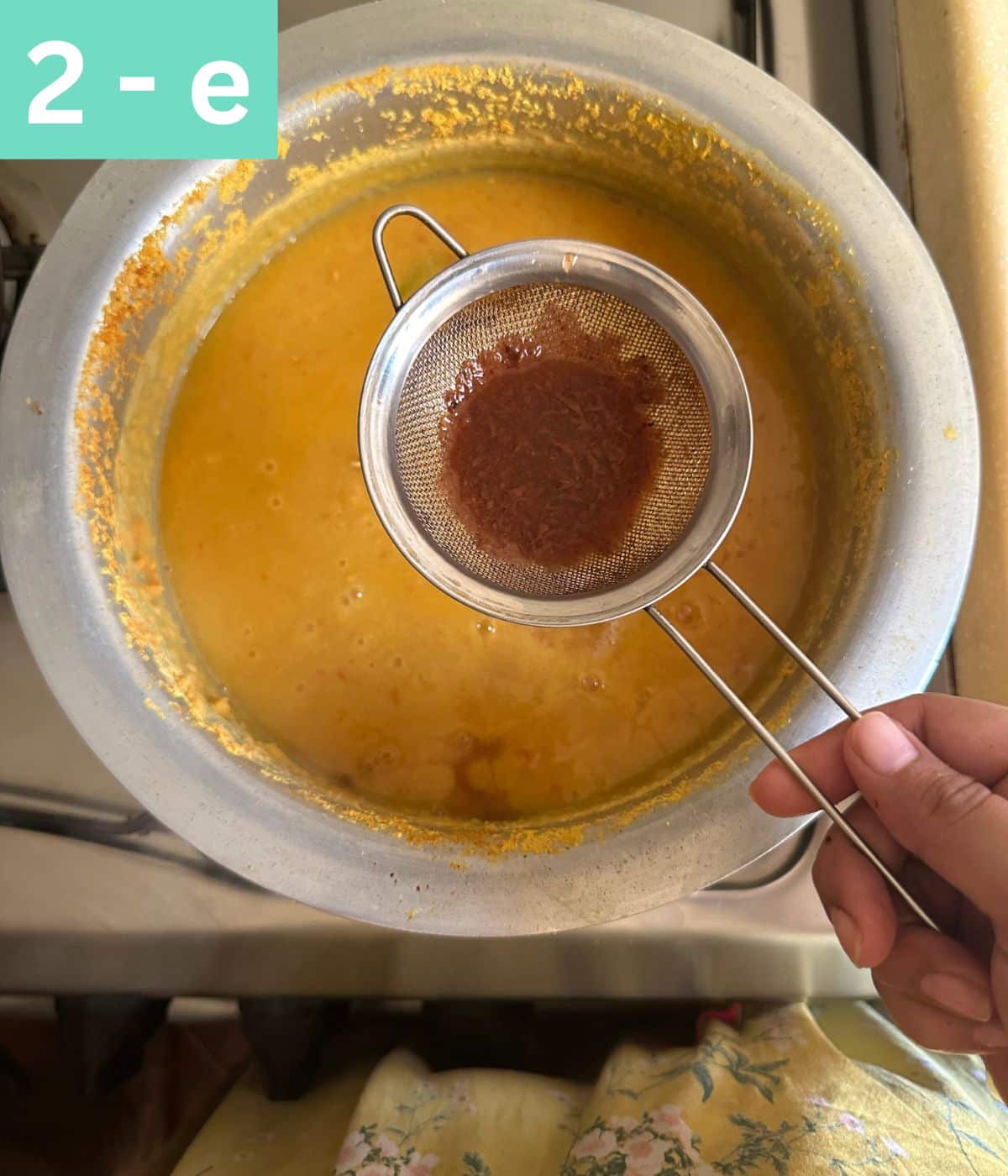 a small tea strainer being used to add tamarind water to dal without impurities.