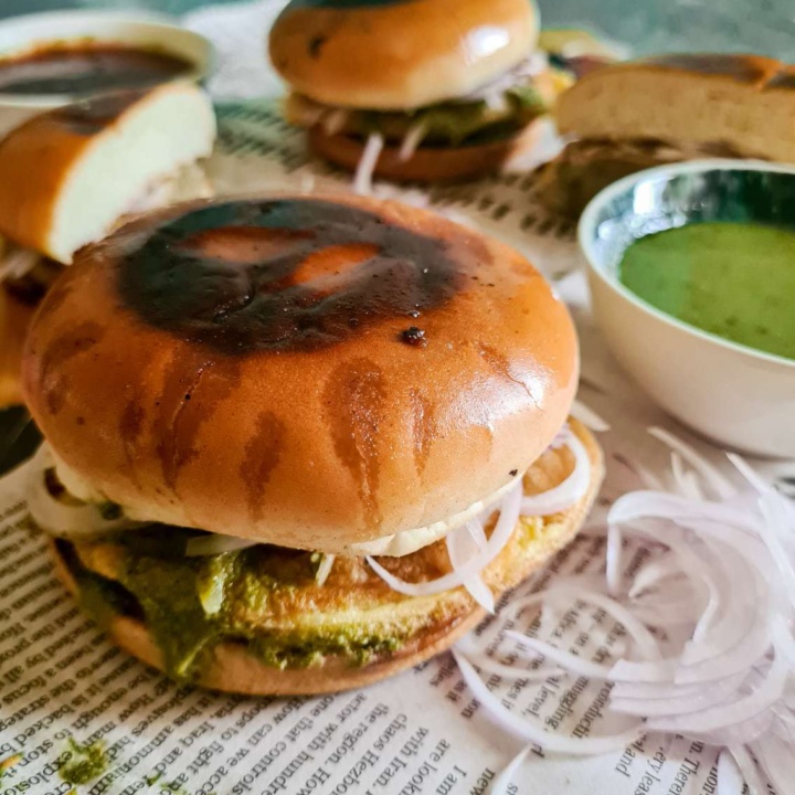 an assembled bun kebab in focus, with 2 in the background, a green chutney and sliced raw onions peaking from the side