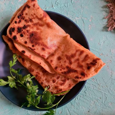a folded square paratha or fried flatbread on a dark blue plate with some coriander on the side.