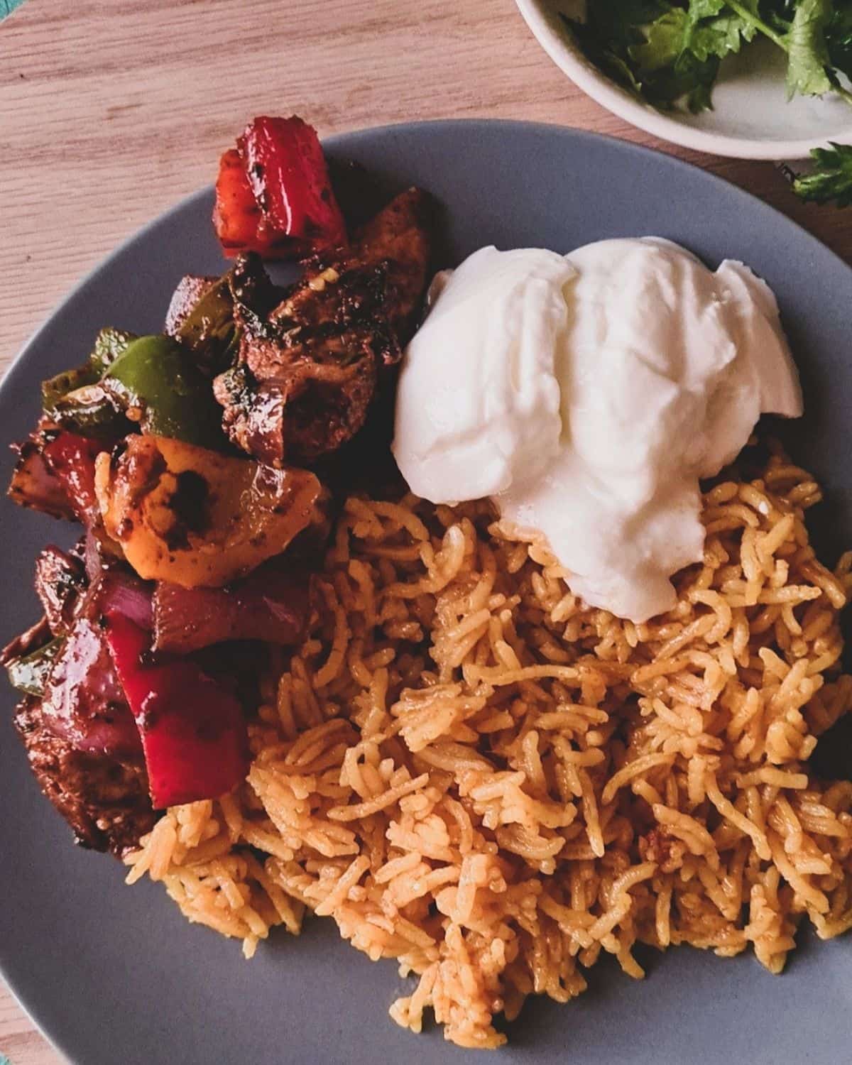 a gray plate holding portions of yellow rice, plain yogurt and spicy chicken stir fry