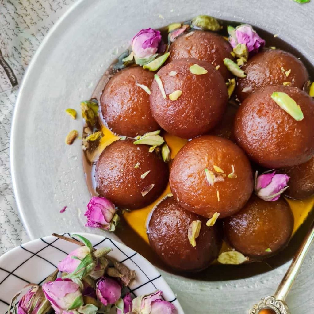 gulab jamuns, a sweet fried milk ball dessert shown garnished with nuts in a silver platter