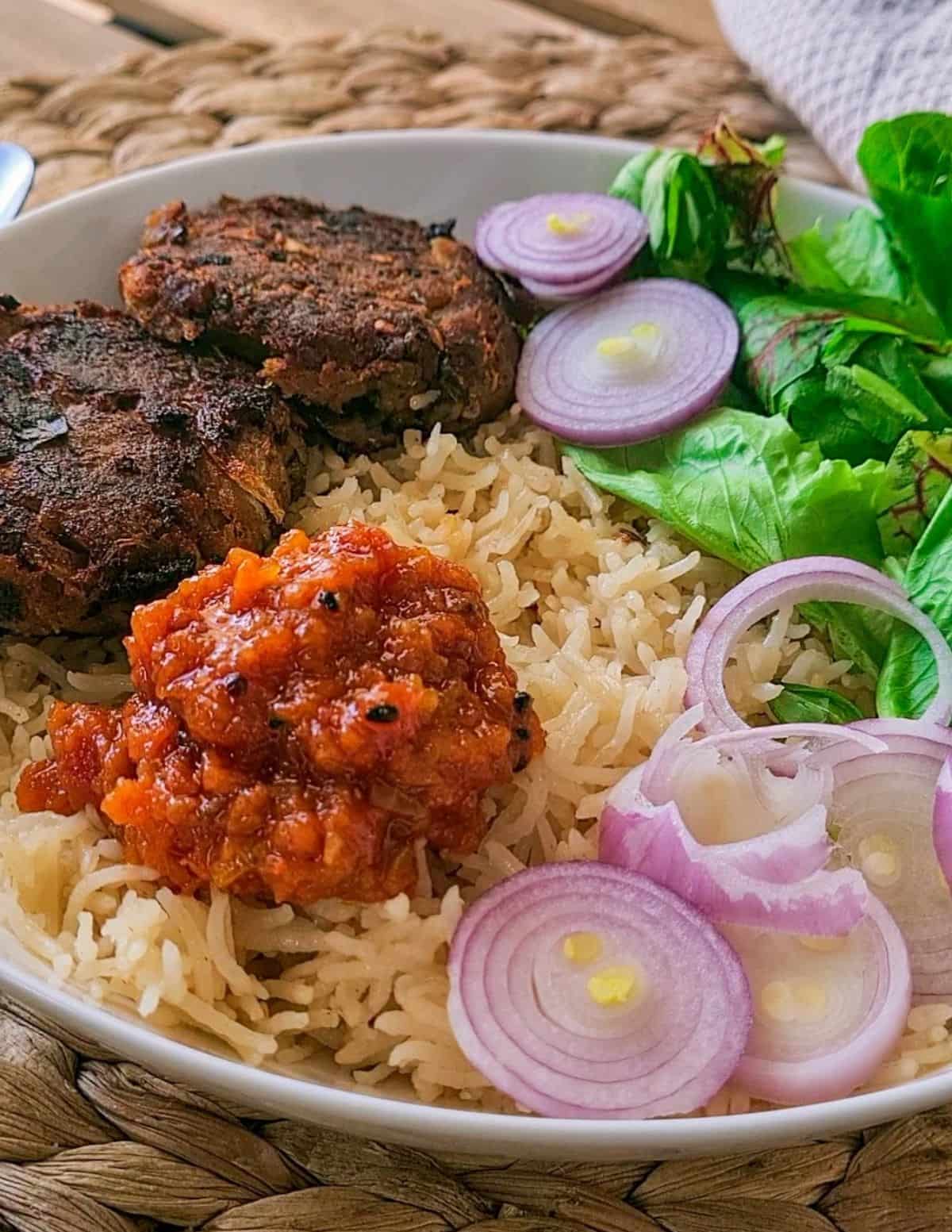 meal showing rice, beef kebabs, raw sliced onions, salad and tomato chutney on the side