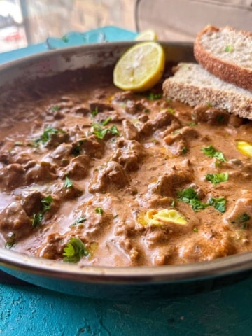 peri peri chicken liver served in a skillet with bread slices and lemon on the side.