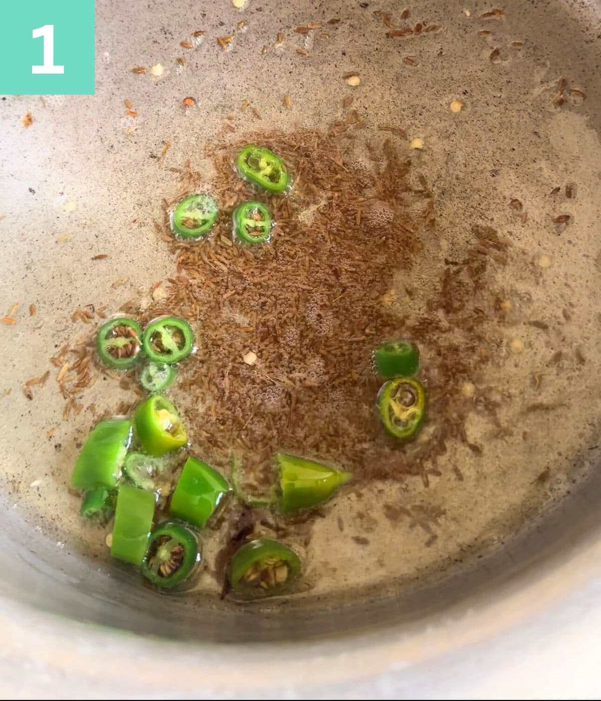 green chilies and cumin seeds in oil in a pot.